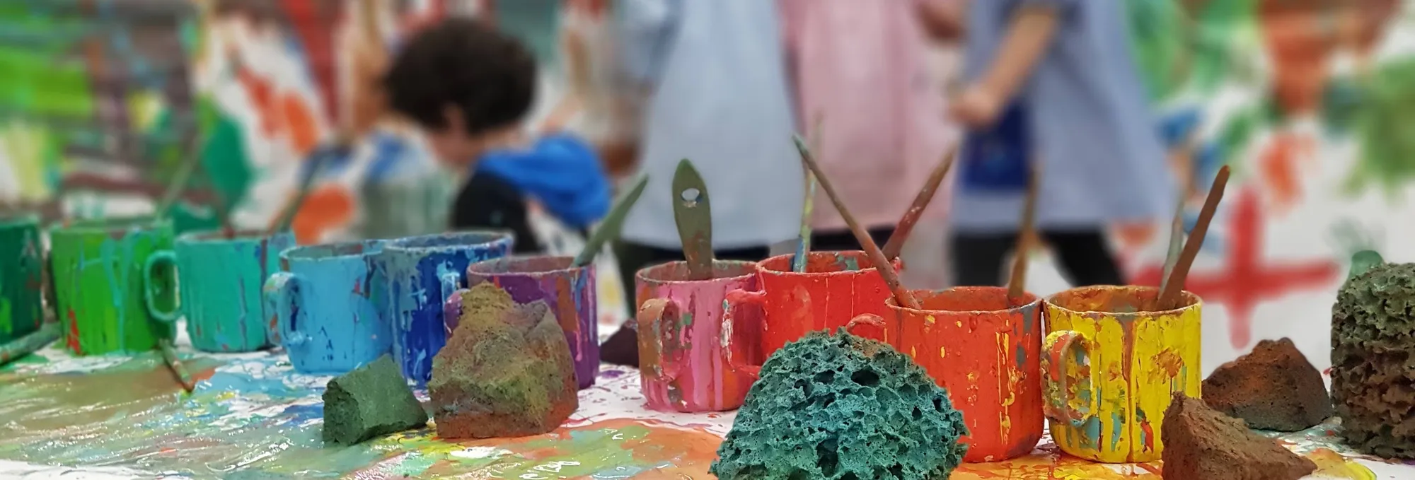 Pots de pintura de colors i esponges en una taula d’un taller